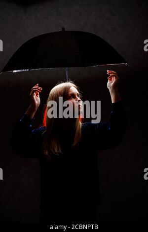 Mädchen steht unter einem Regenschirm vor einem dunklen Hintergrund Stockfoto