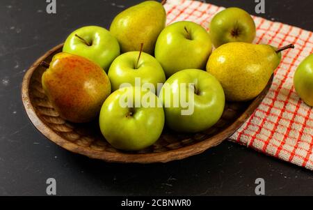 Geschnitzte Holzschale mit Äpfeln und Birnen mit rot kariert Tischdecke auf schwarzem Brett Stockfoto