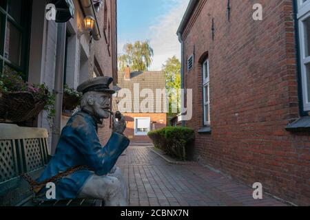 Alte Statue eines Seekapitäns, der eine Pfeife raucht und Sitzen auf einer Bank in einer Stadtstraße Stockfoto