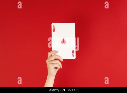 Ass der Herzen, Hand hält Spielkarte vor einem tiefen roten Hintergrund, mit Kopierraum Stockfoto