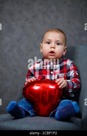 Ein kleiner Junge im Hemd spielt mit einem Ballon In Form eines Herzens Stockfoto