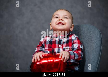 Ein kleiner Junge im Hemd spielt mit einem Ballon In Form eines Herzens Stockfoto