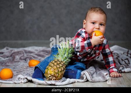 Der kleine Junge im Hemd sitzt auf dem karierten Und hält die Früchte Stockfoto