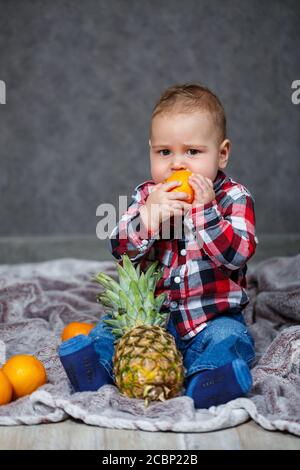 Der kleine Junge im Hemd sitzt auf dem karierten Und hält die Früchte Stockfoto