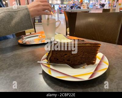 Frau essen traditionelle Sachertorte Schokoladenkuchen oder Torte österreichischer Herkunft - Wasser in der Glastasse mit heißem Tee mischen Stockfoto