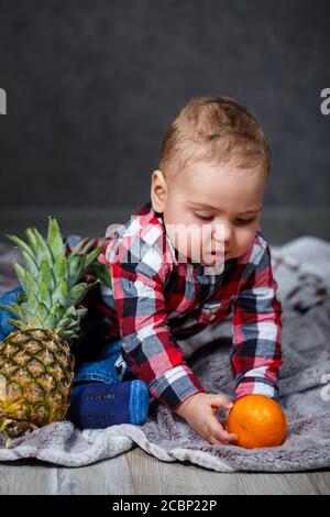 Der kleine Junge im Hemd sitzt auf dem karierten Und hält die Früchte Stockfoto