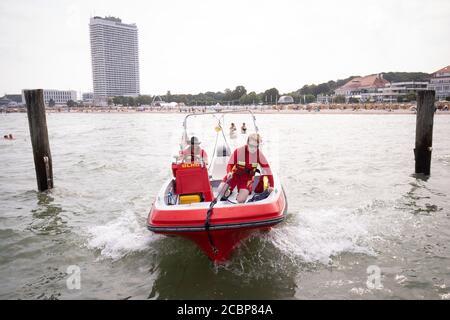 14. August 2020, Schleswig-Holstein, Travemünde: Wilhelm (l.) und Michelle, Bootsführer und Rettungsschwimmer des Deutschen Rettungsschwimmerverbandes (DLRG), legen nach einer Kontrollfahrt am Strand fest. Die Rettungsschwimmer der DLRG an der Ostsee befinden sich in diesem Sommer in einem Dilemma. Die Entfernungsregeln aufgrund der Corona-Pandemie erschwerten Rettungseinsätze, aber trotz der vollen Strände der letzten Tage gab es keine Probleme mit Rettungsaktionen. Foto: Christian Charisius/dpa Stockfoto