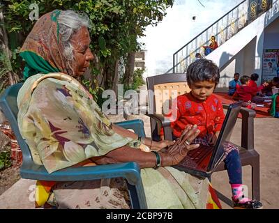 DISTRIKT KATNI, INDIEN - 13. JANUAR 2020: Eine alte Frau aus einem indischen Dorf, die einen Laptop mit kleinen Kindern im Freien betreibt. Stockfoto