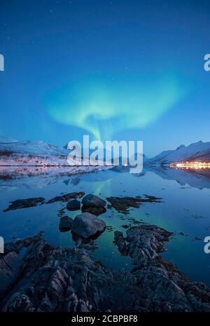 Aurora borealis über schneebedeckten Gipfeln spiegelt sich in einem Fjord, Senja Island, Botnhamn, Troms, Norwegen Stockfoto