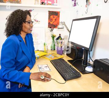 Dunkelhäutig, lächelnde Frau mit Brille arbeitet an ihrem Schreibtisch vor einem Computer, Home Office, Deutschland Stockfoto