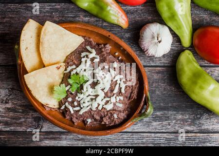 Mexikanische frittierte Bohnen genannt Frijoles Refritos, Platte mit schwarzen Bohnen auf einem Holztisch in Mexiko Stockfoto