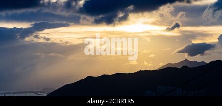 Hohe Berge, die unter dem Sonnenuntergang glitzern und durch die Wolken durchdringen Himmel Stockfoto