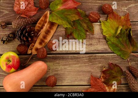 Kürbis, Apfel, Nüsse, Herbstblätter und Tannenzapfen auf einem Holztisch mit Platz für einen Text Stockfoto