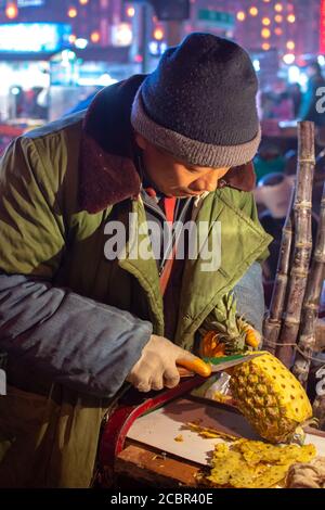 Luoyang, Provinz Henan / China - 3. Januar 2016: Mann schneidet und verkauft frische Ananasscheiben auf der Straße Lebensmittel Obststand in Luoyang, China Stockfoto