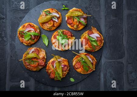 Hausgemachte kleine Pizza mit Pesto, Salami, Tomaten und Rucola auf schwarzem Hintergrund Stockfoto