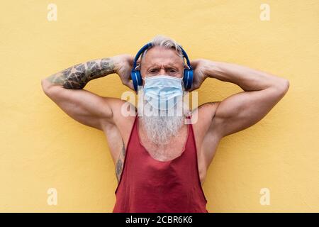 Senior Athlet Mann trägt Gesicht medizinische Maske für Coronavirus Prävention beim Hören Playlist Musik - Reifen Tattoo Kerl nach dem Training duri Stockfoto