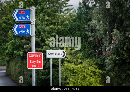 Soziale Distanzierung Covid-19 Zeichen neben einem Friedhof Zeichen Stockfoto