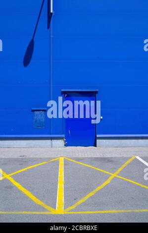 Es gibt keine Parkplätze vor der Tür - der Bereich ist von gelber Farbe durchgestrichen. Minimalistisches Industriegebäude mit blauer Fassade Stockfoto