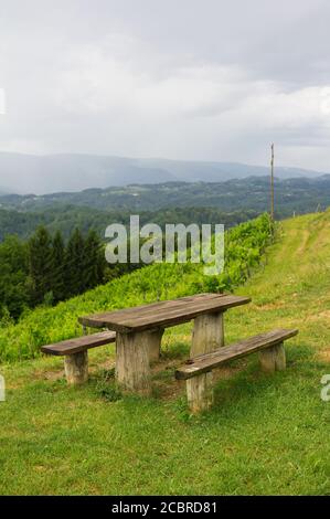 Sveti Urban, Umgebung von Maribor, Slowenien - rustikale Holzbank, Tisch und schöne Natur der slowenischen Landschaft mit Weinberg. Bewölktes Wetter Stockfoto