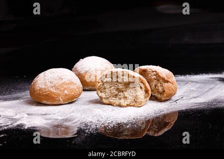 Backen auf schwarzem Hintergrund. Weiße Brötchen mit Pulver und Mehl bestreut. Stockfoto