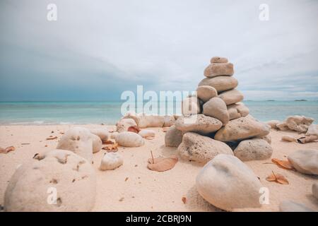 Gestapelte Steine über dem Meer bei Sonnenuntergang. Balancierte Steine zu einem Turm am Strand gestapelt, Wolken mit dramatischem Himmel Stockfoto