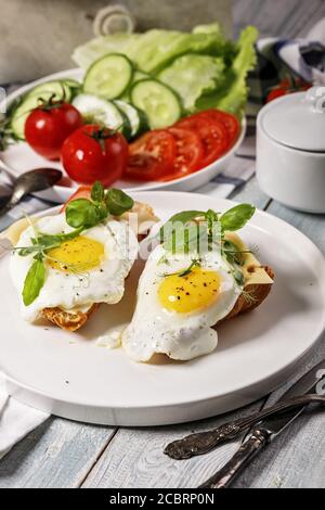 Spiegeleier mit Gewürzen, frischem Basilikum und Kräutern auf einem weißen Teller. Frischer Gurken- und Tomatensalat. Morgendliches Essen Stillleben. Leckeres Frühstück Stockfoto