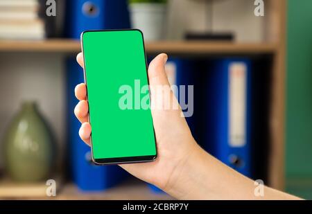 Frau hält grünen Bildschirm Smartphone mit einem Büro Hintergrund Stockfoto