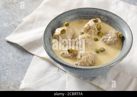 Königsberger Klopse oder gekochte Fleischbällchen in einer weißen Bechamelsauce mit Kapern, traditionelles polnisches und deutsches Gericht in einer grauen Schüssel auf einer weißen Serviette, s Stockfoto