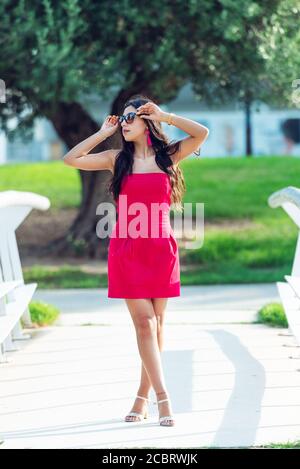 Stehende Mädchen junge Latina, langhaarige Brünette in rotem Kleid mit gekreuzten Beinen. Modekonzept Stockfoto