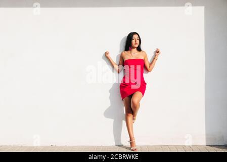 Porträt von eleganten lateinischen jungen Mädchen mit langen Brünette Haare und rotes Kleid auf weißer Wand mit starken Schatten, Blick auf die Kamera. Kopieren Raum Stockfoto