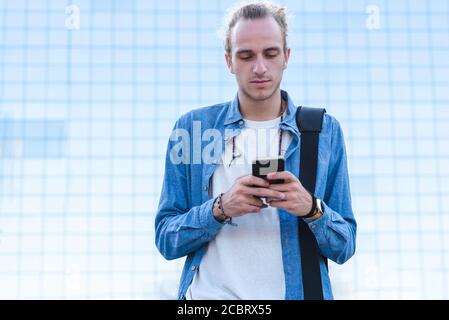 Schlank kaukasischen Mann Dressing lässig und mit Telefon mit einem Bürogebäude aus Glas im Hintergrund Stockfoto