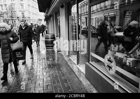 Lviv/Ukraine - 30. Januar 2020: An einem regnerischen Wintertag laufen die Bürger auf der Akademika Hnatyuka Straße entlang des Bürgerwegs, was sich in der Vitrine widerspiegelt Stockfoto