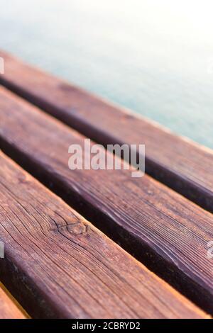 Schräge Holzdeck eines Anlegesteg am Gardasee. Die Sonne spiegelt sich im Wasser. Das Holz ist warm, braun gefärbt. Detail, Makrobild mit Bokeh. Stockfoto