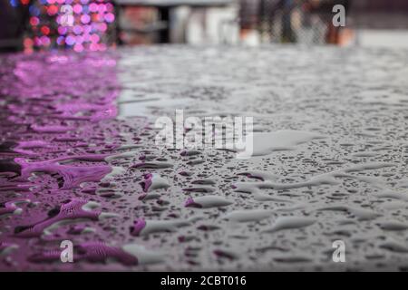 Textur. Tropfen oder kleine Wasserpfützen nach dem Regen auf einer glatten matten Oberfläche von dunkler Farbe, die das Licht der Beleuchtung reflektiert. Stockfoto