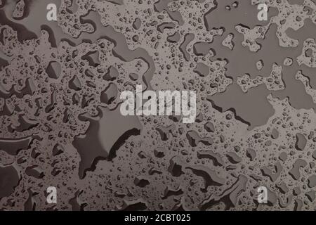 Hintergrund. Tropfen oder kleine Wasserpfützen nach Regen auf eine glatte matte Oberfläche von dunkler Farbe. Stockfoto