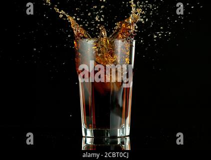 Spritzendes Cola-Getränk aus Glas, isoliert auf schwarzem Hintergrund. Frisches Sommergetränk, Frostbewegung. Stockfoto