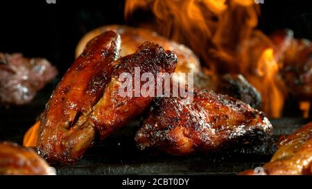 Hühnerfleischstücke auf dem Grill. Beine und Flügel Fleisch auf Grillrost mit Feuer platziert. Schwarzer Hintergrund. Stockfoto