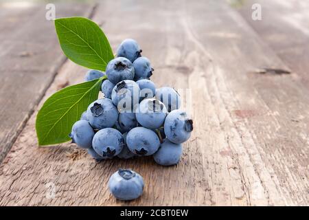 Schöne Heidelbeeren mit grünen Blättern auf einem alten Holztisch Stockfoto
