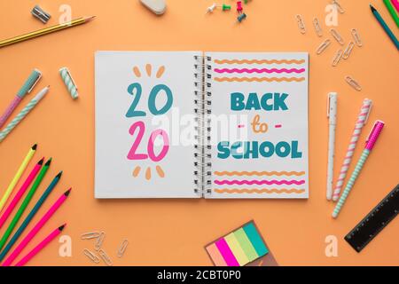 Stock Foto des Back to School Konzept mit einem Offenes Notizbuch mit Schriftzügen und einigen Schreibwaren auf einem Lachshintergrund Stockfoto