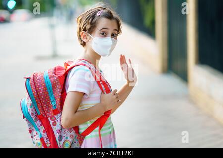 Neun Jahre altes Mädchen geht zurück in die Schule mit einer Maske und einer Schultasche. Stockfoto