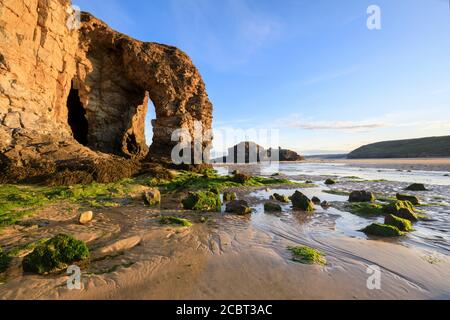 Der natürliche Meeresbogen und der Chapel Rock am Perranporth Beach in Cornwall wurden an einem Morgen Mitte Juli mit Sandmustern als Vordergrund-Interesse aufgenommen. Stockfoto