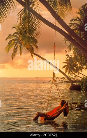 Frau in Schaukel Stuhl hängen von Palme auf Meeru Island auf den Malediven bei Sonnenaufgang Stockfoto
