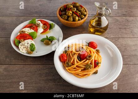 Kompletter Tisch mit italienischen Gerichten auf Tellern. Spaghetti, Caprese, Oliven und Olivenöl. Stockfoto