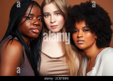 Junge hübsche kaukasische, afro, skandinavische Frau posiert fröhlich zusammen auf braunem Hintergrund, Lifestyle diverse Nationalität Menschen Konzept Stockfoto