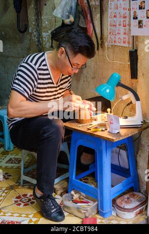 Hanoi, Vietnam - 20 2019. April: Der Mann, der Holz-Souvenirs in seinem Geschäft verarbeitet. Stockfoto