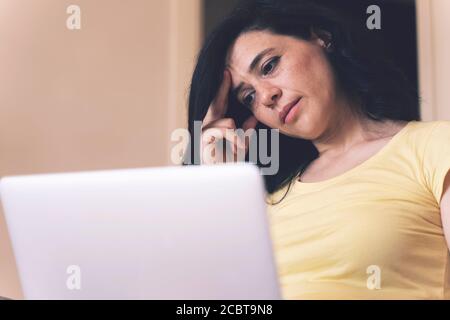 Abgelenkt von der Arbeit besorgt junge Frau sitzt auf der Couch mit Laptop, denken an Probleme. Nachdenkliche unmotivierte Dame, die Laptop anschaut, Mangel fühlt Stockfoto
