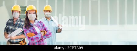 Weibliche und männliche Auftragnehmer in harten Hüten tragen medizinische Gesichtsmasken auf der Baustelle während Coronavirus Pandemie Banner. Stockfoto