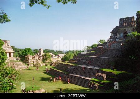 Der Turm des Palastkomplexes in der Ferne. Gruppe des Kreuzes, Vordergrund. Kreuzentempel (rechts); Sonnentempel (links). Menschen in der frühen Morgensonne. Palenque Maya Ruinen. Chiapas, Mexiko. Vintage Film Bild - ca. 1990. Nicht identifizierbare Personen. Stockfoto