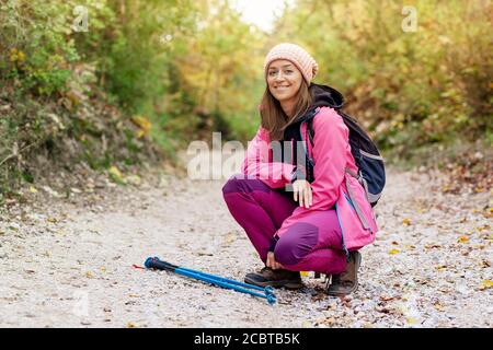 Hiker Mädchen hocken auf einem breiten Weg in den Bergen. Rucksacktourist mit rosa Jacke in einem Wald. Gesunder Fitness-Lebensstil im Freien. Stockfoto