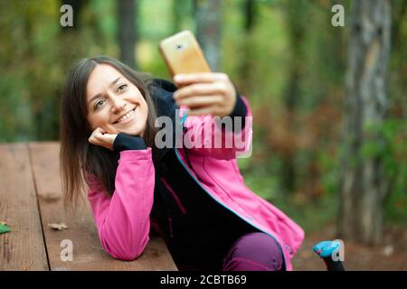 Wanderer Mädchen auf einer Bank im Wald ruhen. Backpacker mit rosa Jacke nimmt Selfie mit Smartphone. Stockfoto